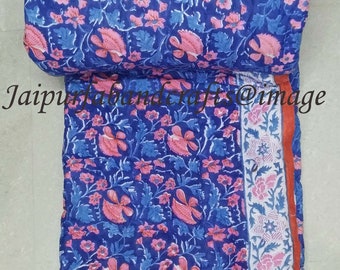 May include: A blue and pink floral patterned cotton quilt with a white and pink border and an orange trim. The quilt is folded in half and is lying on a white surface.
