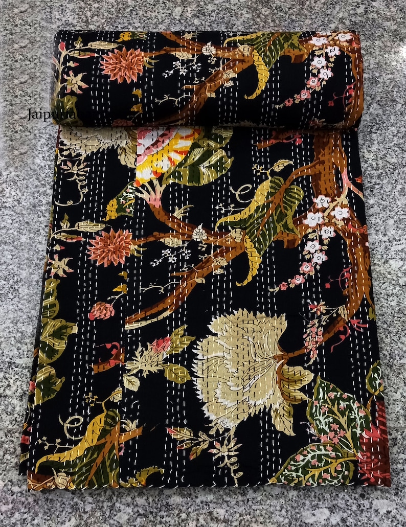 May include: Black kantha quilt with a floral pattern featuring brown branches, green leaves, and pink and yellow flowers. The quilt is hand-stitched with white thread.