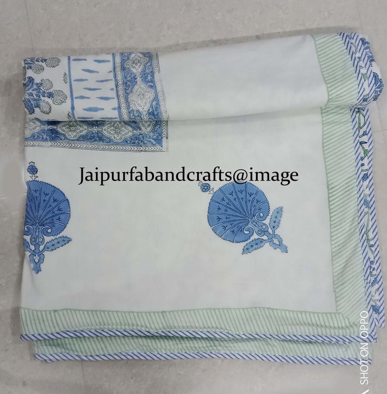 May include: White cotton bed sheet with a blue and green floral print. The sheet has a green and white striped border. The text "Jaipurfabandcrafts@image" is printed on the sheet.