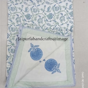 May include: A white cotton quilt with a blue and green floral print. The quilt has a light green border with white stripes. The quilt is folded in half and the inside of the quilt has a blue and white floral print.