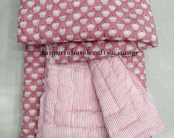 May include: A pink and white cotton quilt with a floral print on one side and white stripes on the other side. The quilt is folded in half and the floral side is facing up. The quilt is made in India.