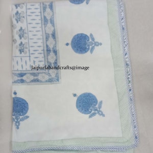 May include: White cotton fabric with a blue and white floral print. The fabric has a green border with a white stripe. The text "jaipurfabandcrafts@image" is printed on the fabric.