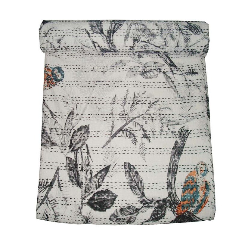 May include: A white kantha quilt with a black and gray floral pattern. The quilt is rolled up at the top and has a decorative stitch pattern.