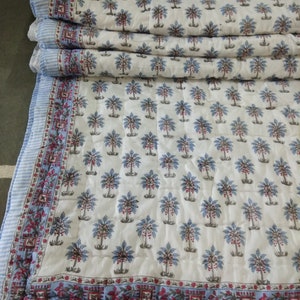 Op de afbeelding: Een wit katoenen dekbed met een blauw en rood bloemenpatroon. Het dekbed is in drie&euml;n gevouwen en heeft een blauw-wit gestreepte rand.