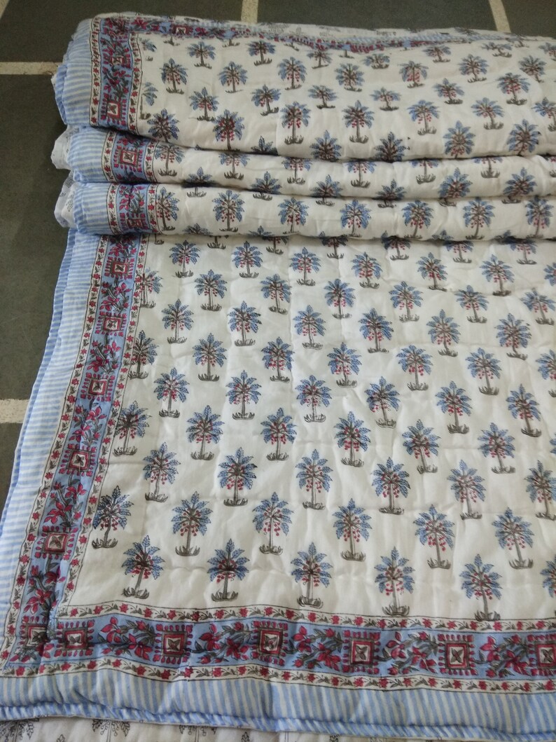 Op de afbeelding: Een wit katoenen dekbed met een blauw en rood bloemenpatroon. Het dekbed is in drie&euml;n gevouwen en heeft een blauw-wit gestreepte rand.