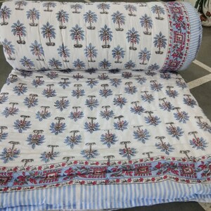 Op de afbeelding: Wit katoenen dekbed met een blauwe en bruine bloemenprint. Het dekbed heeft een blauw-wit gestreepte rand met een rood-wit bloemenpatroon.