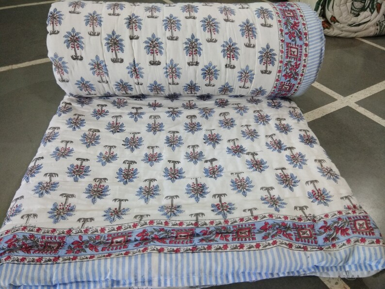 Op de afbeelding: Wit katoenen dekbed met een blauwe en bruine bloemenprint. Het dekbed heeft een blauw-wit gestreepte rand met een rood-wit bloemenpatroon.