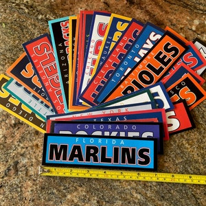 Può includere: Una collezione di adesivi colorati di squadre di baseball con nomi di squadre e loghi, tra cui i San Diego Padres, gli Angeles Angels, gli Arizona Diamondbacks, i Chicago Cubs, i Milwaukee Brewers, gli Indians di Cleveland, i Toronto Blue Jays, i Baltimore Orioles, i New York Yankees, i Texas Rangers, i Colorado Rockies, i Florida Marlins e i San Francisco Giants.