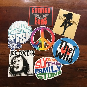 May include: A collection of vintage music band stickers featuring a peace sign, a fish, a target, and band names like "The Who", "Sly and the Family Stone", "Jethro Tull", "Joe Cocker", and "Canned Heat".