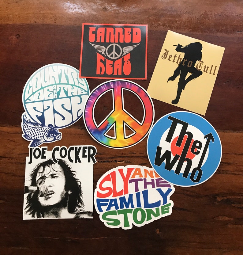 May include: A collection of vintage music band stickers featuring a peace sign, a fish, a target, and band names like "The Who", "Sly and the Family Stone", "Jethro Tull", "Joe Cocker", and "Canned Heat".