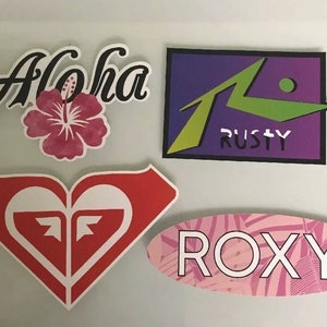 May include: Four colorful stickers with various designs. The stickers feature the words "Aloha", "ROXY", and "RUSTY". One sticker features a red heart with a white "F" inside.
