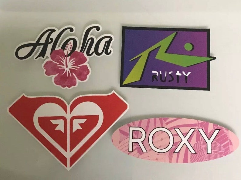 May include: Four colorful stickers with various designs. The stickers feature the words "Aloha", "ROXY", and "RUSTY". One sticker features a red heart with a white "F" inside.