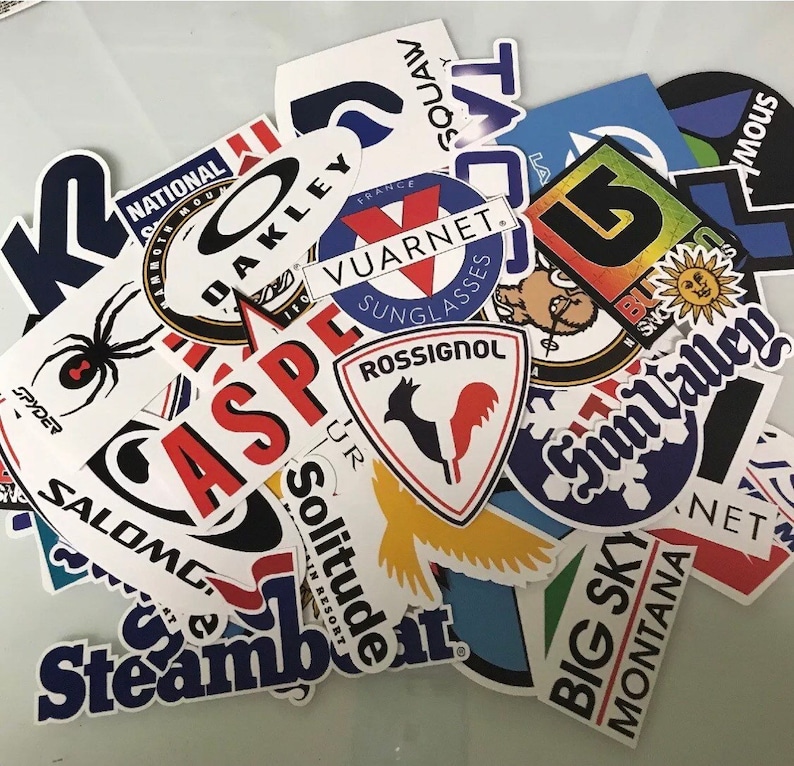 May include: A collection of colorful stickers featuring various ski resort and brand logos, including "Aspen", "Vuarnet", "Rossignol", "Big Sky Montana", "Steamboat", and "Sun Valley".