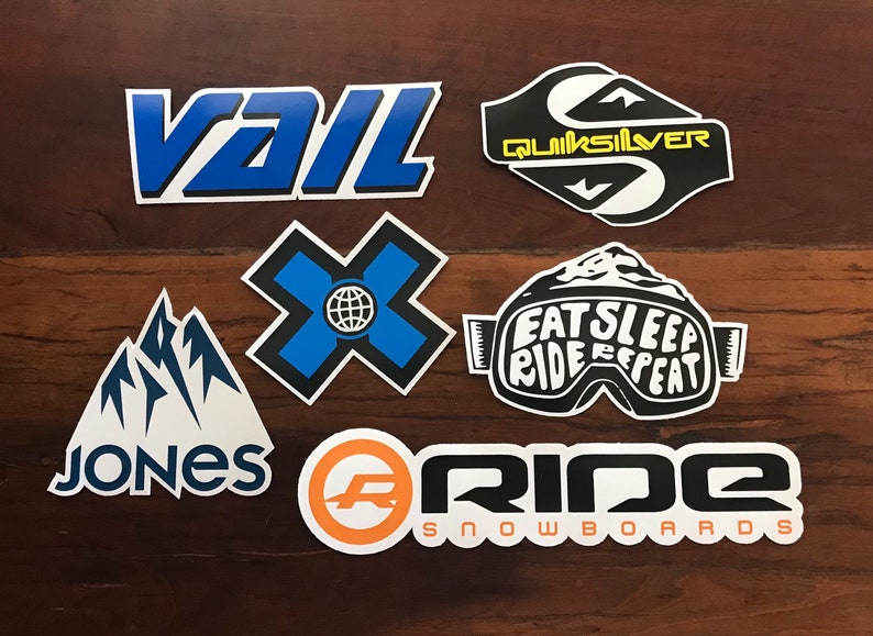 Puede incluir: Una colecci&oacute;n de siete pegatinas de snowboard de colores. Las pegatinas presentan logotipos de marcas como Vail, Quiksilver, Jones, Ride Snowboards, y una pegatina con el texto "Eat Sleep Ride Repeat" en unas gafas.