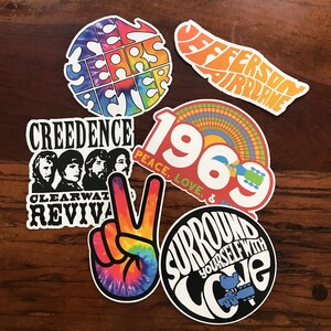 May include: A set of six vintage-style stickers featuring psychedelic designs and text. The stickers include the words "Ten Years After", "Jefferson Airplane", "Creedence Clearwater Revival", "1969 Peace, Love, &", "Surround Yourself With Love", and a peace sign with a tie-dye pattern.