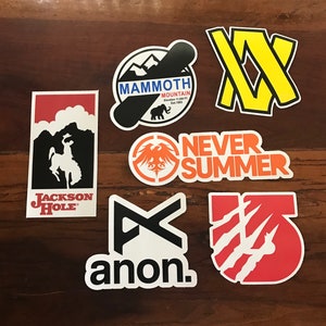 Puede incluir: Una colecci&oacute;n de nueve pegatinas coloridas con varios logotipos y dise&ntilde;os. Las pegatinas incluyen logotipos para Mammoth Mountain, Jackson Hole, Anon, Never Summer y algunas otras marcas. Las pegatinas est&aacute;n todas sobre una superficie de madera.