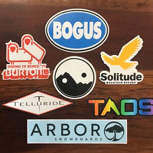 Puede incluir: Una colecci&oacute;n de pegatinas coloridas con varios logotipos de estaciones de esqu&iacute;, incluyendo "Bogus", "Telluride", "Taos", "Solitude Mountain Resort", "Arbor Snowboards" y "Burton Snowboards".