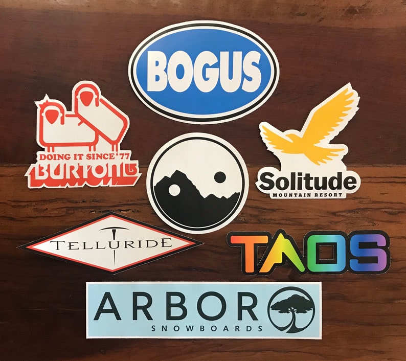 Puede incluir: Una colecci&oacute;n de pegatinas coloridas con varios logotipos de estaciones de esqu&iacute;, incluyendo "Bogus", "Telluride", "Taos", "Solitude Mountain Resort", "Arbor Snowboards" y "Burton Snowboards".