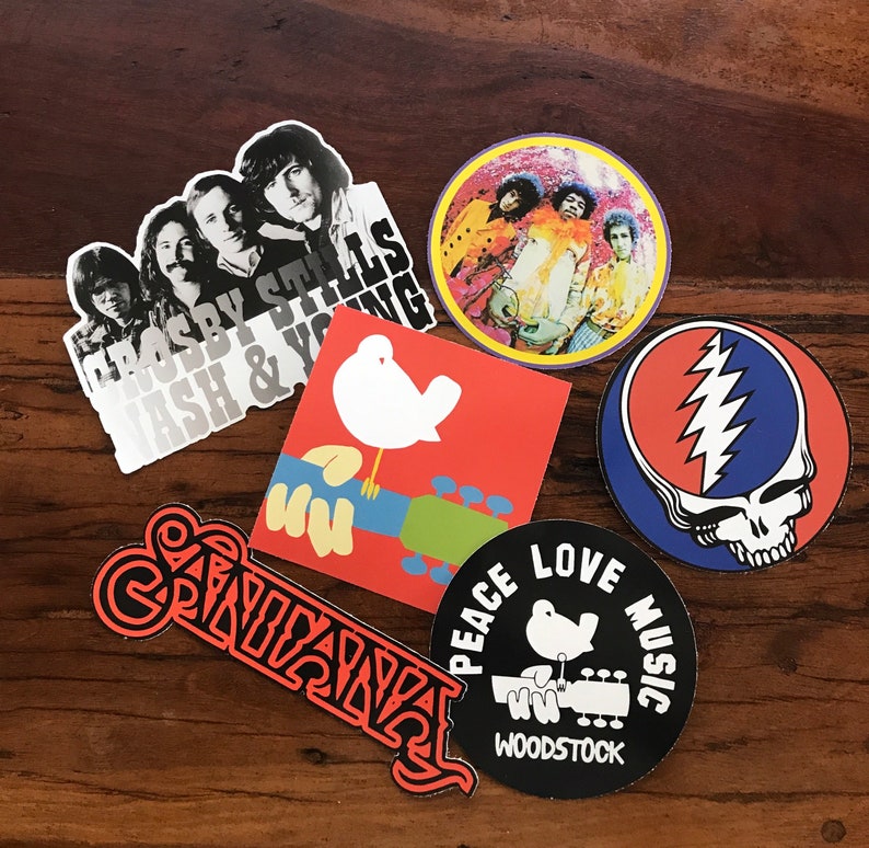 May include: A collection of eight vintage music-themed stickers. The stickers feature various musicians, bands, and music festivals, including Crosby, Stills & Nash, The Grateful Dead, and Woodstock. The stickers are printed on a white background with colourful designs.