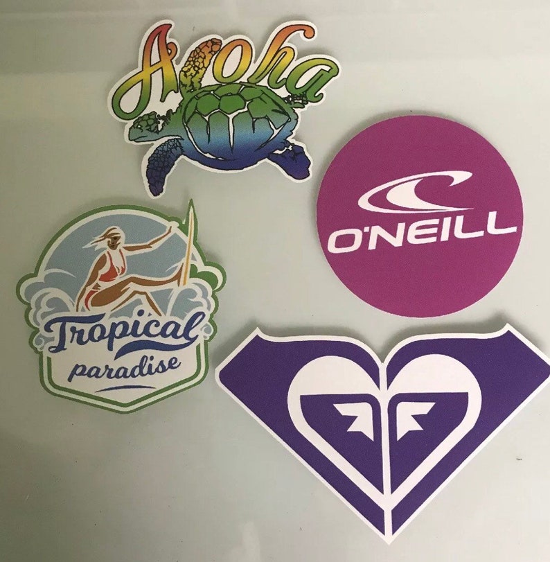 May include: Four colorful stickers with different designs. The first sticker is a rainbow colored turtle with the word "Aloha" above it. The second sticker is a purple circle with the word "O'Neill" and a white wave logo. The third sticker is a green and white sticker with a woman surfing and the words "Tropical paradise". The fourth sticker is a purple heart with a white wave logo.