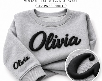 May include: A light grey crewneck sweatshirt featuring the name Olivia in a black 3D puff print on the centre chest and on the left sleeve. A circular inset shows a close-up of the raised black lettering texture on the grey fabric.