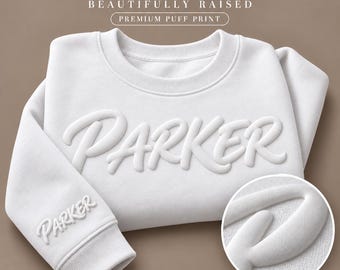 May include: A white crewneck sweatshirt featuring the name PARKER in a raised, white puff print across the chest and on the sleeve cuff. The text YOUR NAME BEAUTIFULLY RAISED PREMIUM PUFF PRINT appears above the sweatshirt, with a circular detail.