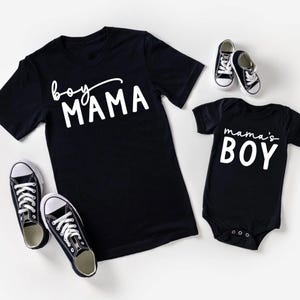May include: Black t-shirts and a baby onesie with white text that reads "boy MAMA" and "mama's BOY". Two pairs of black and white sneakers are also in the image. The items are likely for a mother and son.