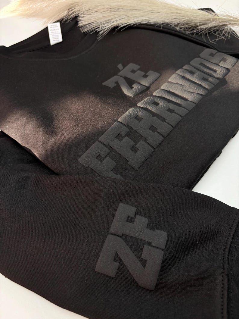 以下が含まれることがあります： 胸元にマットブラックの立体的な質感で「Z&Eacute; FERRINHOS」の文字が施された黒の長袖スウェットシャツ。袖には同じマットブラックの立体的な素材で「ZF」の文字があしらわれており、全体的にモノクロームな外観に仕上がっています。