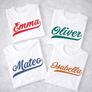 Può includere: Quattro magliette bianche, ciascuna piegata e con un nome diverso in un carattere corsivo. I nomi sono Emma in rosso, Oliver in verde, Mateo in blu e Isabella in arancione. Le magliette sono disposte su una superficie chiara.