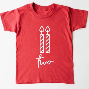 Puede incluir: Camiseta roja de manga corta con texto blanco y un gr&aacute;fico de dos velas. El texto dice "dos".