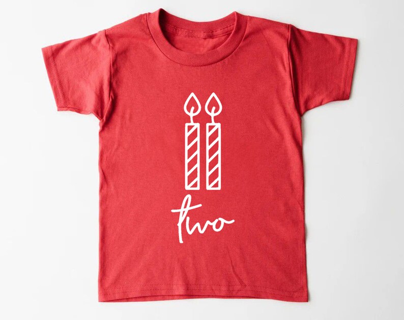 Puede incluir: Camiseta roja de manga corta con texto blanco y un gr&aacute;fico de dos velas. El texto dice "dos".