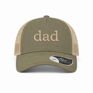 Può includere: Cappellino da camionista verde oliva con la parola "dad" ricamata in beige chiaro. Il cappellino ha un retro in rete e una visiera curva. Una piccola etichetta con testo è attaccata alla visiera.
