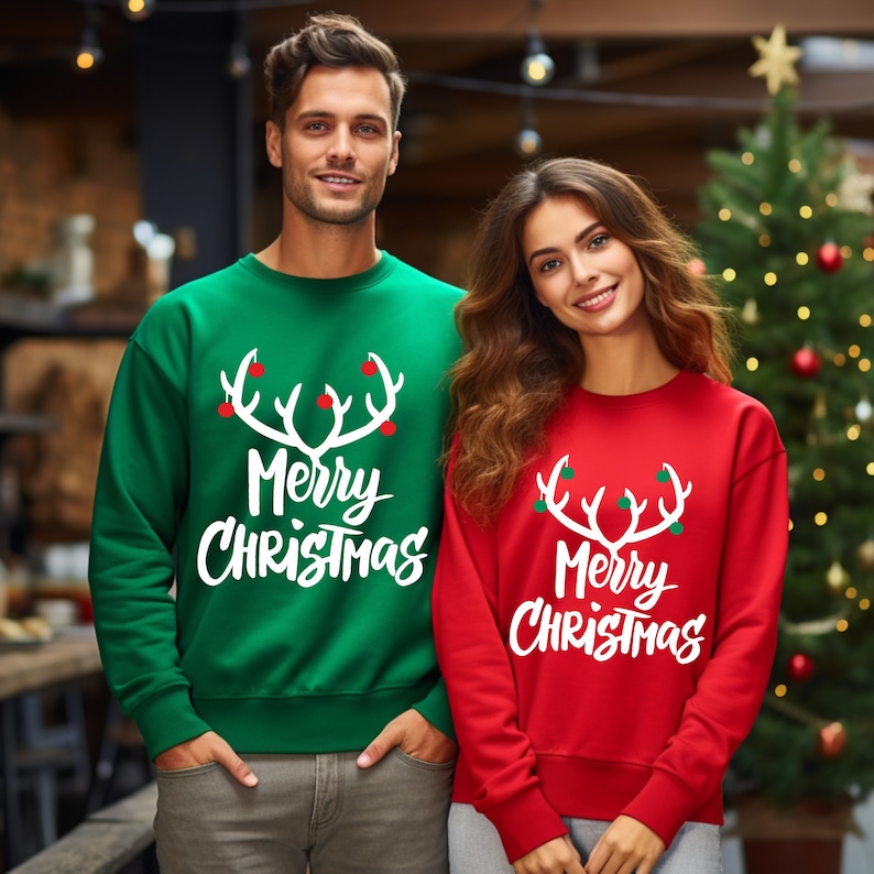 May include: Green and red crewneck sweatshirts with the text "Merry Christmas" and a white antler design. The sweatshirts are worn by two people in front of a Christmas tree.