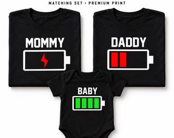 May include: A matching set of three black garments including two t-shirts and one baby bodysuit. The shirts feature the text MOMMY and DADDY above battery icons with red lightning and bars. The bodysuit features BABY above a full green battery.