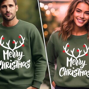 May include: Green sweatshirt with a white antler design and the words "Merry Christmas" in white. The antlers have red ball accents. The sweatshirt is a crew neck style.