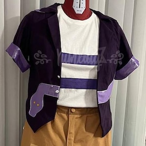 Può includere: Un completo costume con una giacca viola a maniche corte con dettagli viola, una maglietta bianca con una striscia viola e pantaloni color cachi con toppe colorate. La giacca presenta ricami decorativi. I pantaloni hanno una vestibilità ampia.