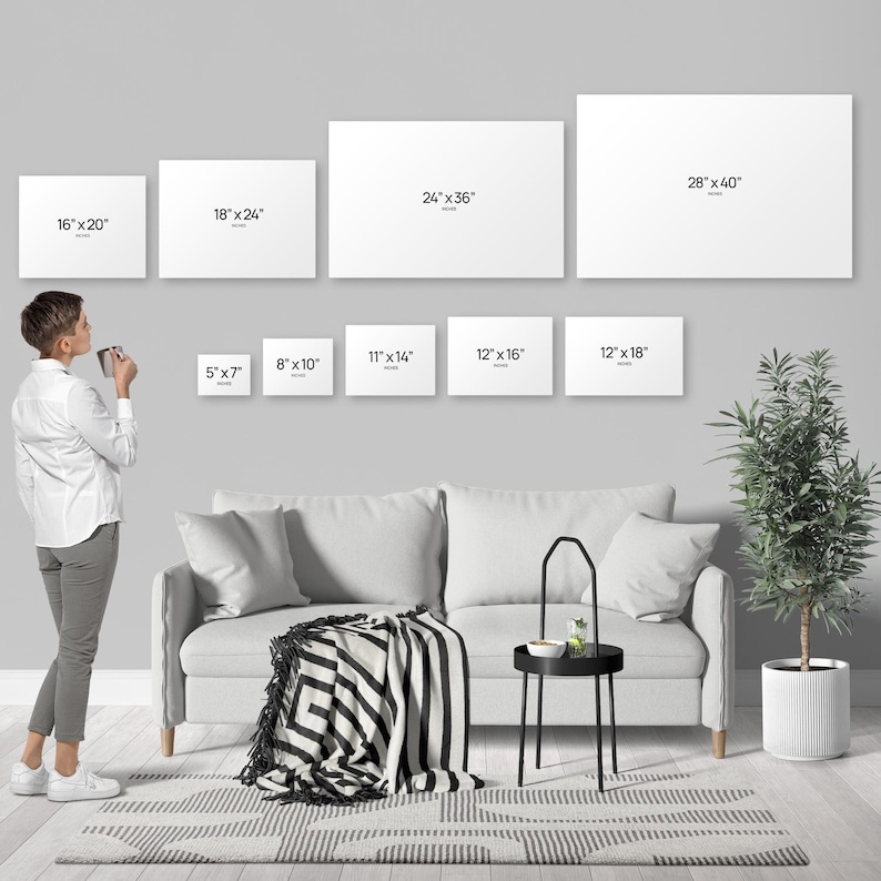 A person standing in a living room, looking at a wall with multiple blank canvas prints of different sizes, and a couch, a coffee table, and a potted plant in the background.