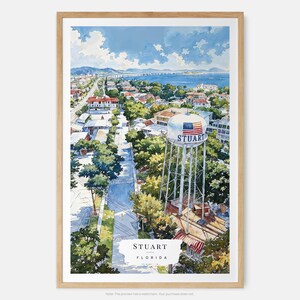 May include: Watercolor print of Stuart, Florida, featuring a detailed aerial view of the town. The image showcases a water tower with the town's name and an American flag, a bridge, and lush greenery. The artwork is framed in a light wood.