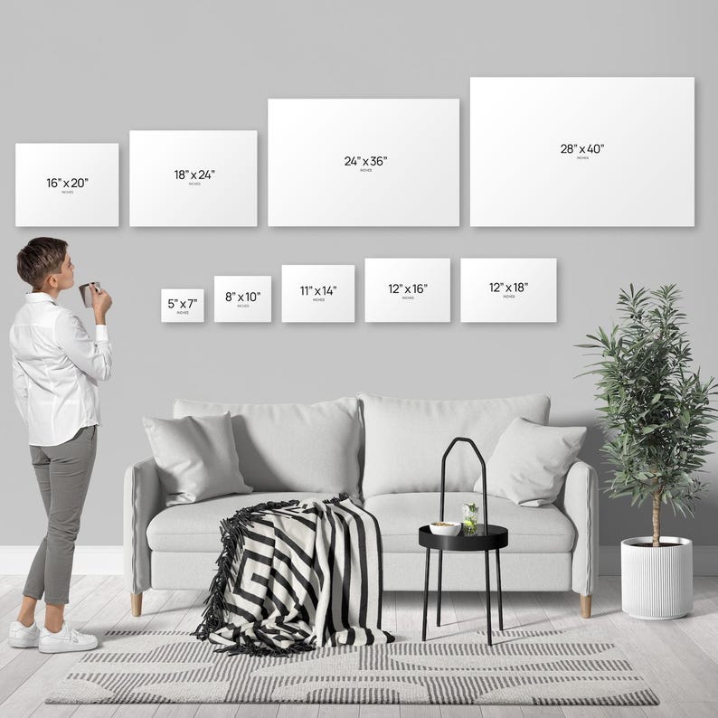 A person standing in a living room, looking at a wall with multiple blank canvas prints of different sizes, and a couch, a coffee table, and a potted plant in the background.
