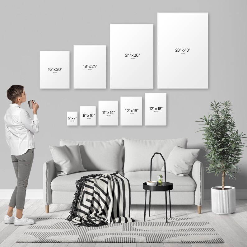 A woman is standing in a living room, looking at a wall with a series of white canvas prints of varying sizes, each labeled with its corresponding dimensions.