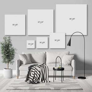 a modern living room with a gray sofa, a black and white striped blanket, and a black floor lamp. Above the sofa, there are five white square frames with black text indicating the size of the frames, ranging from 48 inches to 48 inches.
