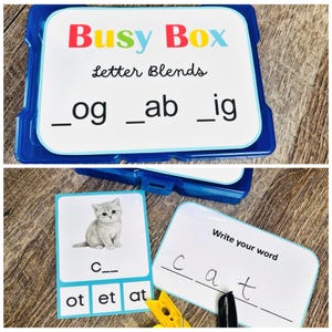 Puede incluir: Una Busy Box azul de pl&aacute;stico con combinaciones de letras, incluyendo "_og", "_ab" e "_ig". La caja contiene tarjetas con una imagen de gatito y la palabra "cat", junto con letras. Tambi&eacute;n se ve un clip amarillo.