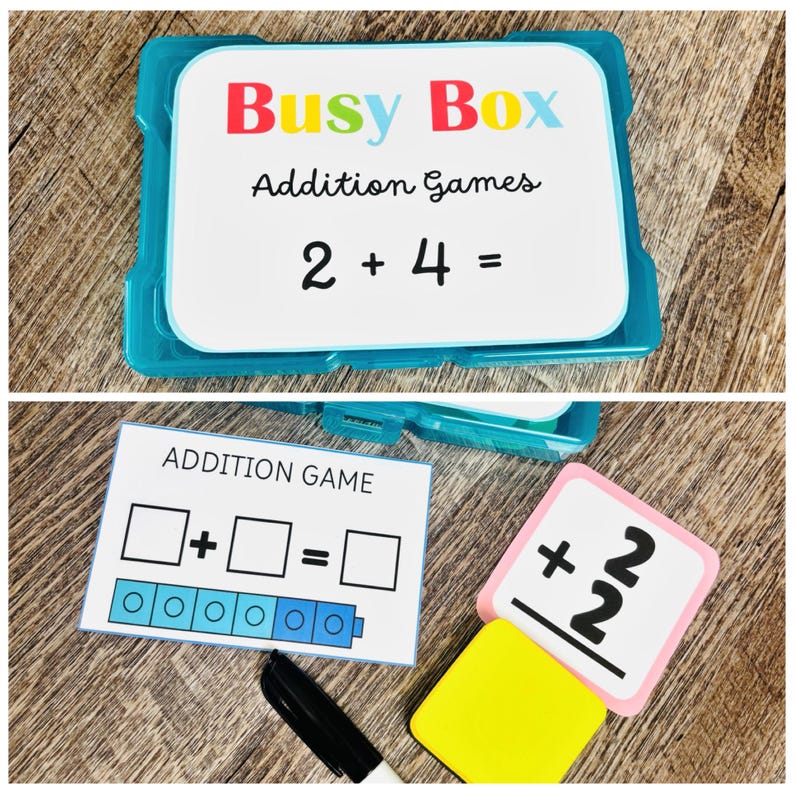 Puede incluir: Un contenedor de pl&aacute;stico azul con la etiqueta "Busy Box Addition Games" con la ecuaci&oacute;n 2 + 4 = mostrada. Tarjetas adicionales muestran un juego de suma con casillas y una tarjeta num&eacute;rica con el n&uacute;mero 2. Tambi&eacute;n se ve un marcador negro y una goma de borrar amarilla.