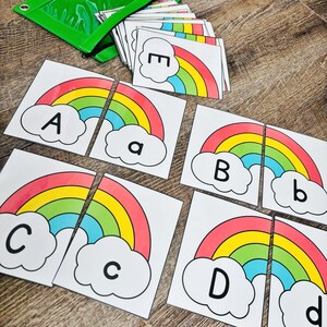 May include: Educational alphabet matching game featuring rainbow-themed cards. Each card has a colorful rainbow design with a letter, both uppercase and lowercase. A green zippered pouch holds the cards, perfect for learning.