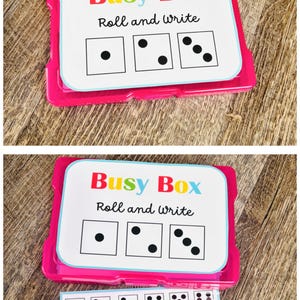 Puede incluir: Un juego educativo rosa y blanco llamado "Busy Box" con el texto "Roll and write". El juego incluye tarjetas con patrones de dados y un dado rojo. La tarjeta inferior muestra palabras CVC.