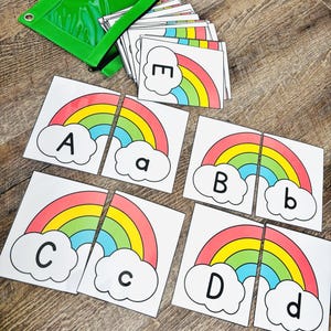 May include: Educational rainbow puzzle cards with letters A, B, C, D, and E. Each card features a colorful rainbow design and a cloud with a letter. A green zippered pouch holds additional cards.