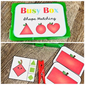Puede incluir: Una caja de pl&aacute;stico verde con una tapa blanca que dice "Busy Box Shape Matching". La tapa presenta ilustraciones de manzanas en forma de tri&aacute;ngulo, c&iacute;rculo y coraz&oacute;n. Se ven tarjetas de emparejamiento y una pinza roja.