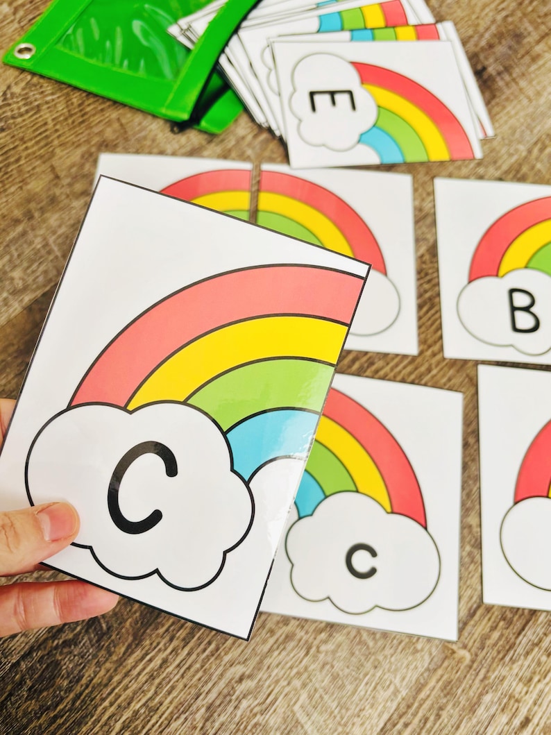 May include: Educational flashcards featuring colorful rainbows and letters. The cards have a white background with a rainbow design in red, orange, yellow, green, and blue. Each card has a letter in a cloud.