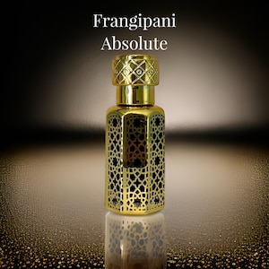 Può includere: Una bottiglia dorata con un design decorativo intricato e un tappo dorato. La bottiglia è piena di un liquido scuro e il testo "Frangipani Absolute" è stampato sull'etichetta.