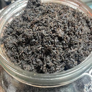 Könnte beinhalten: Ein klares Glasgefäß gefüllt mit dunkelbraunem, zerkleinertem Material. Das Glas hat einen Metallverschluss und einen durchsichtigen Deckel. Der Inhalt scheint lockere, getrocknete Kräuter oder Teeblätter zu sein.